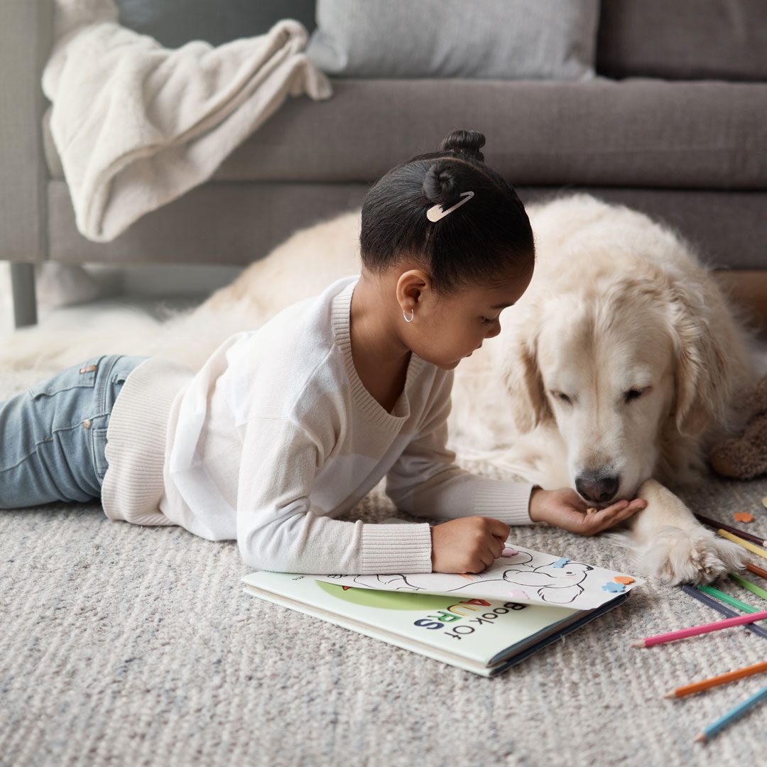 young girl laying on the floor coloring next to her dog